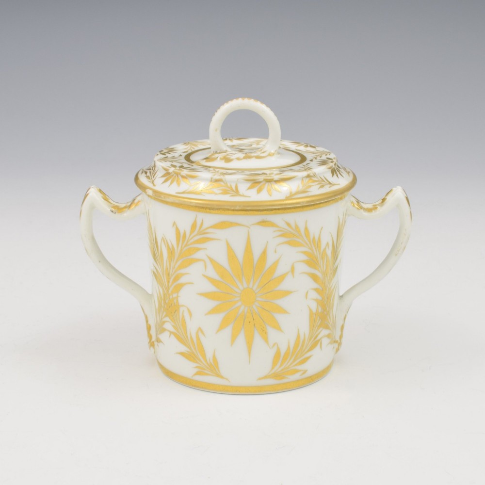 A white Regency period Bloor Derby porcelain chocolate cup featuring twin handles, a fitted lid with a loop finial, hand-painted sepia putti, and gold gilded leaf borders. View IV