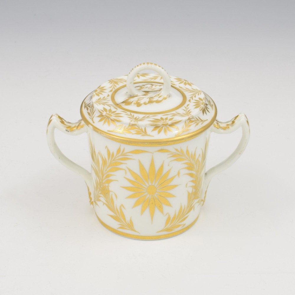 A white Regency period Bloor Derby porcelain chocolate cup featuring twin handles, a fitted lid with a loop finial, hand-painted sepia putti, and gold gilded leaf borders. View V