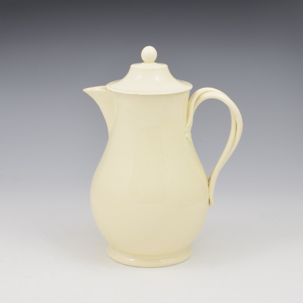 An 18th-century creamware hot water jug featuring a baluster-shaped earthenware body, a fitted dome cover with a ball finial, and a loop handle.