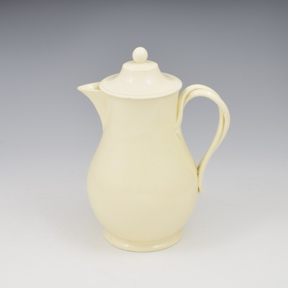 An 18th-century creamware hot water jug featuring a baluster-shaped earthenware body, a fitted dome cover with a ball finial, and a loop handle. View II
