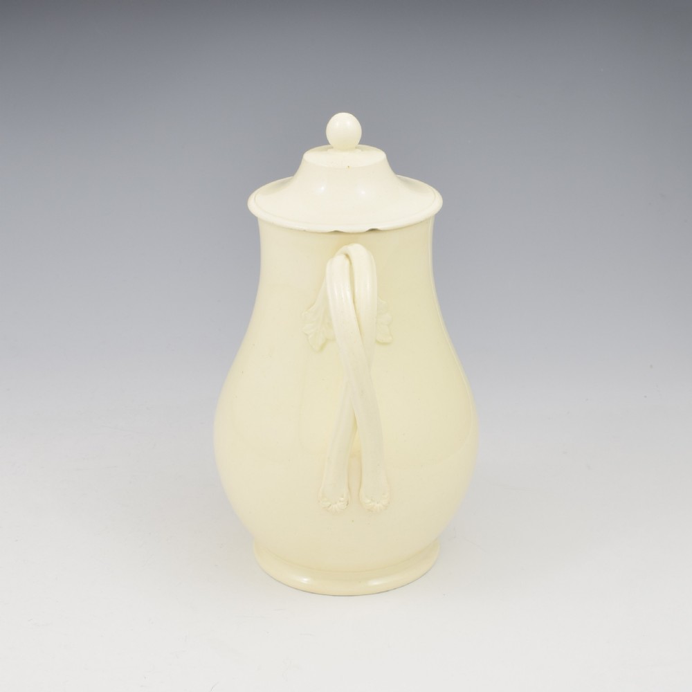 An 18th-century creamware hot water jug featuring a baluster-shaped earthenware body, a fitted dome cover with a ball finial, and a loop handle. View IV
