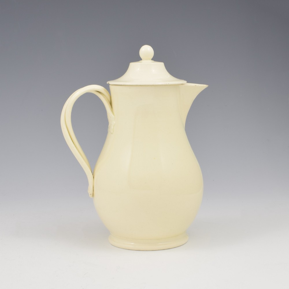 An 18th-century creamware hot water jug featuring a baluster-shaped earthenware body, a fitted dome cover with a ball finial, and a loop handle. View VII