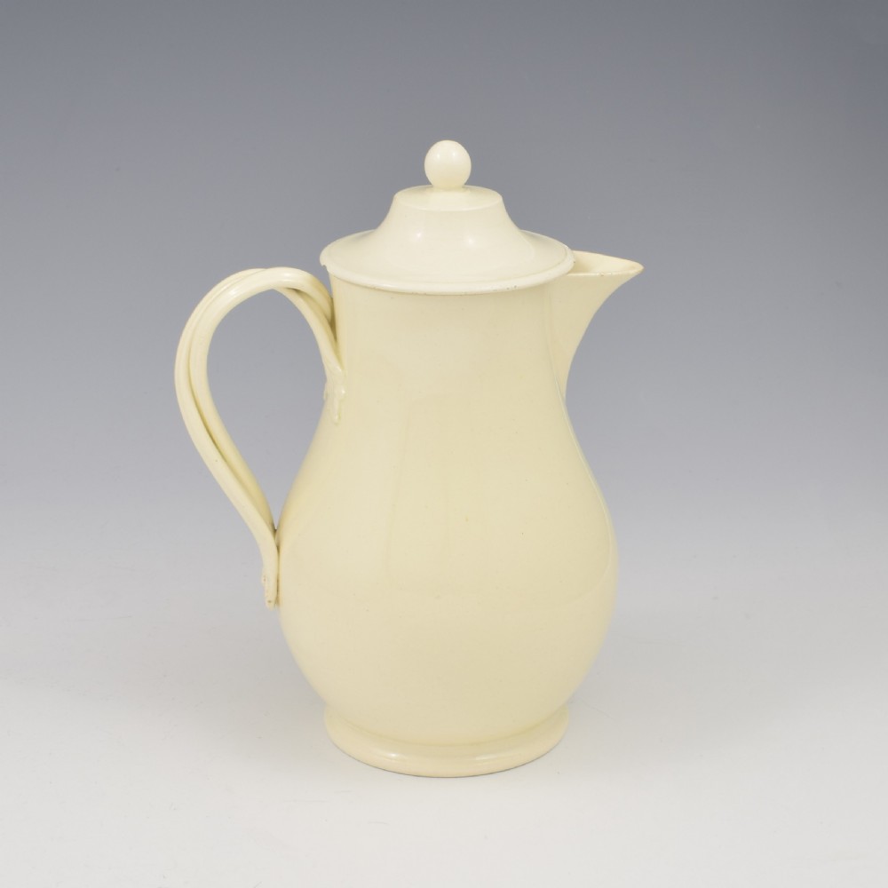 An 18th-century creamware hot water jug featuring a baluster-shaped earthenware body, a fitted dome cover with a ball finial, and a loop handle. View VIII