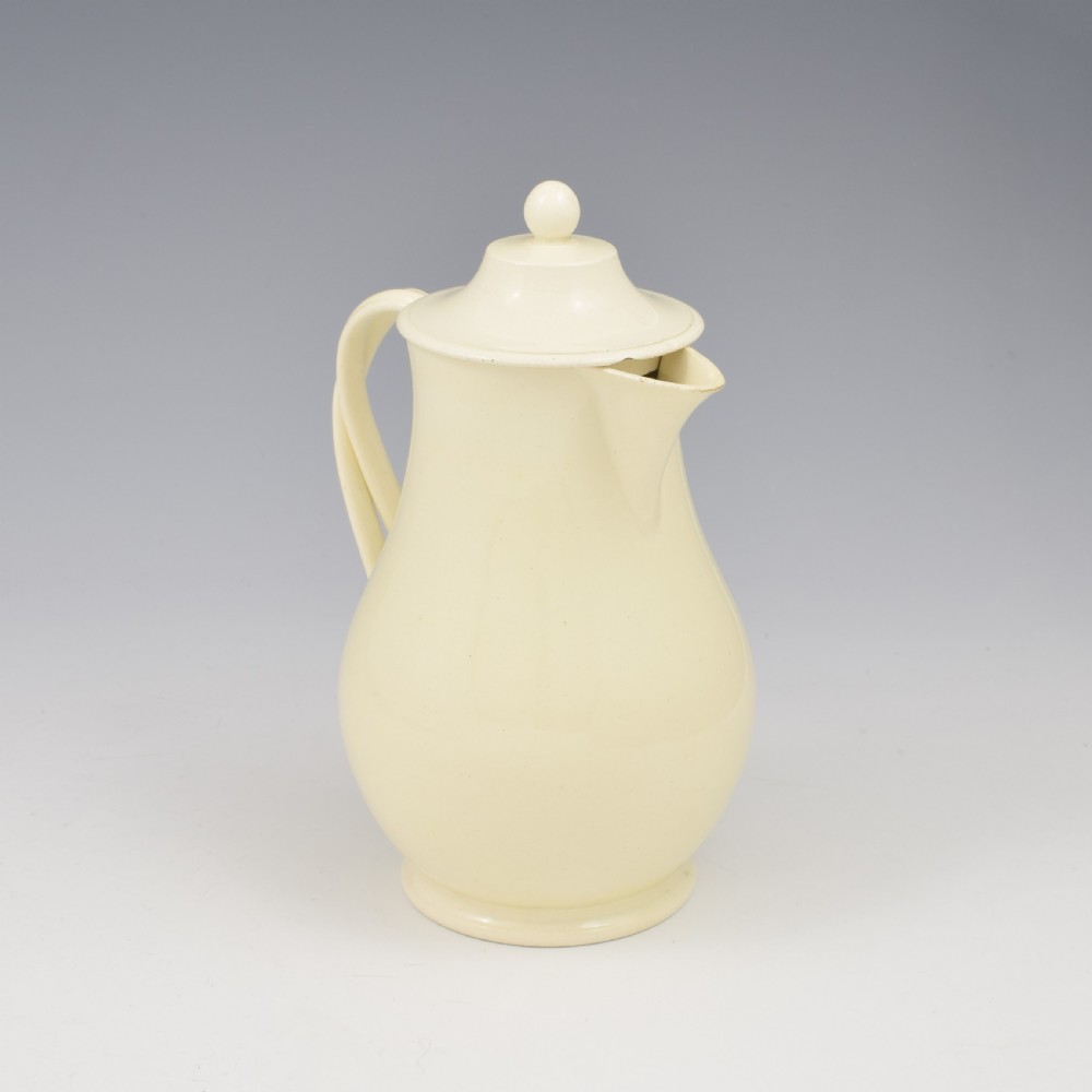 An 18th-century creamware hot water jug featuring a baluster-shaped earthenware body, a fitted dome cover with a ball finial, and a loop handle. View IX