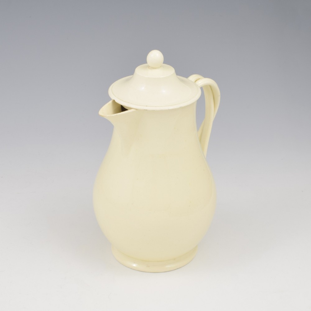 An 18th-century creamware hot water jug featuring a baluster-shaped earthenware body, a fitted dome cover with a ball finial, and a loop handle. View XI