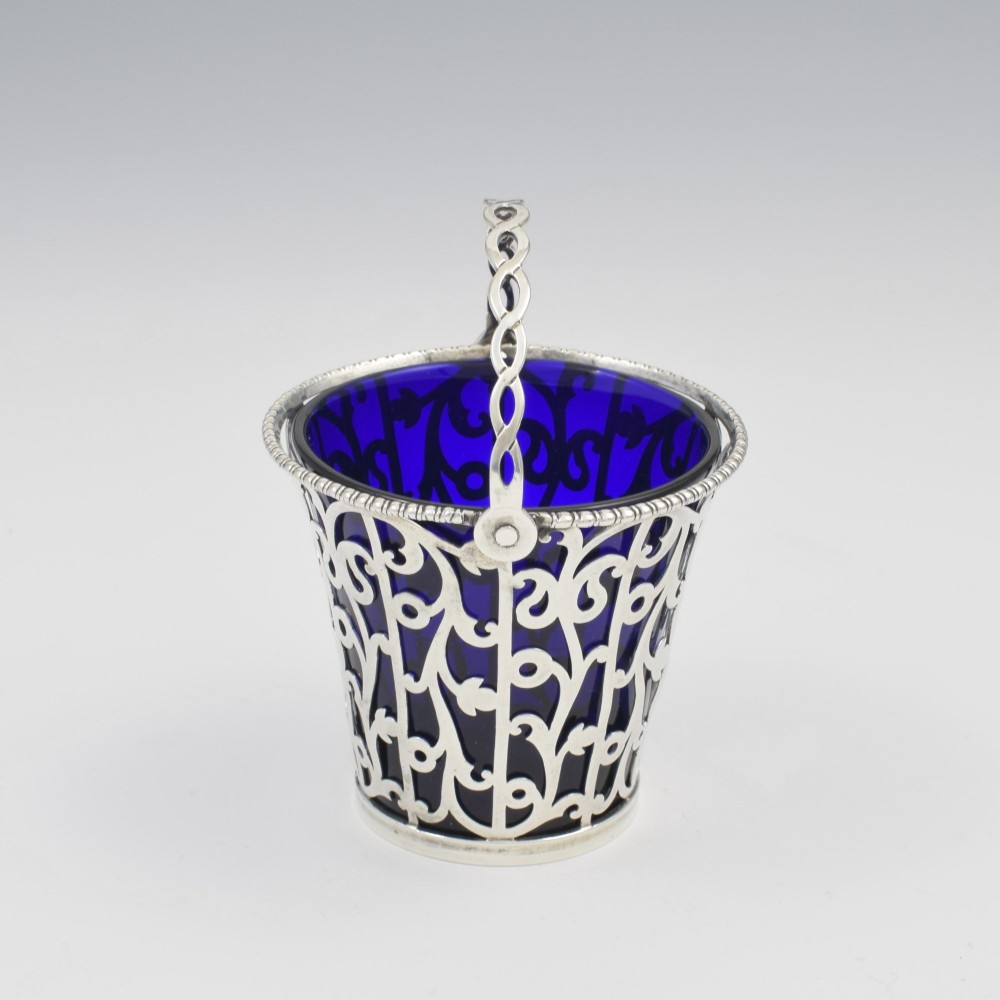 An 18th-century Georgian pierced sterling silver cream pail featuring intricate foliage scrollwork, a swing handle, and a removable cobalt blue glass liner. View III