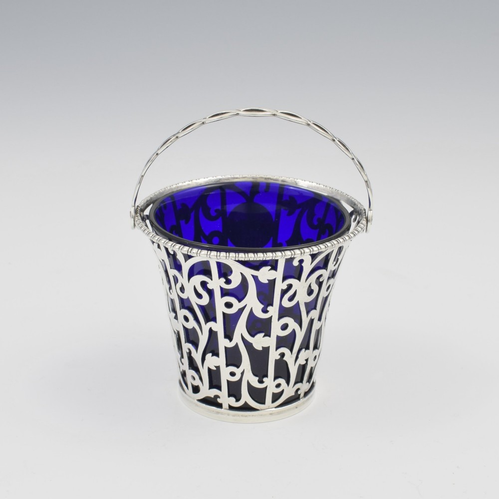 An 18th-century Georgian pierced sterling silver cream pail featuring intricate foliage scrollwork, a swing handle, and a removable cobalt blue glass liner. View IV