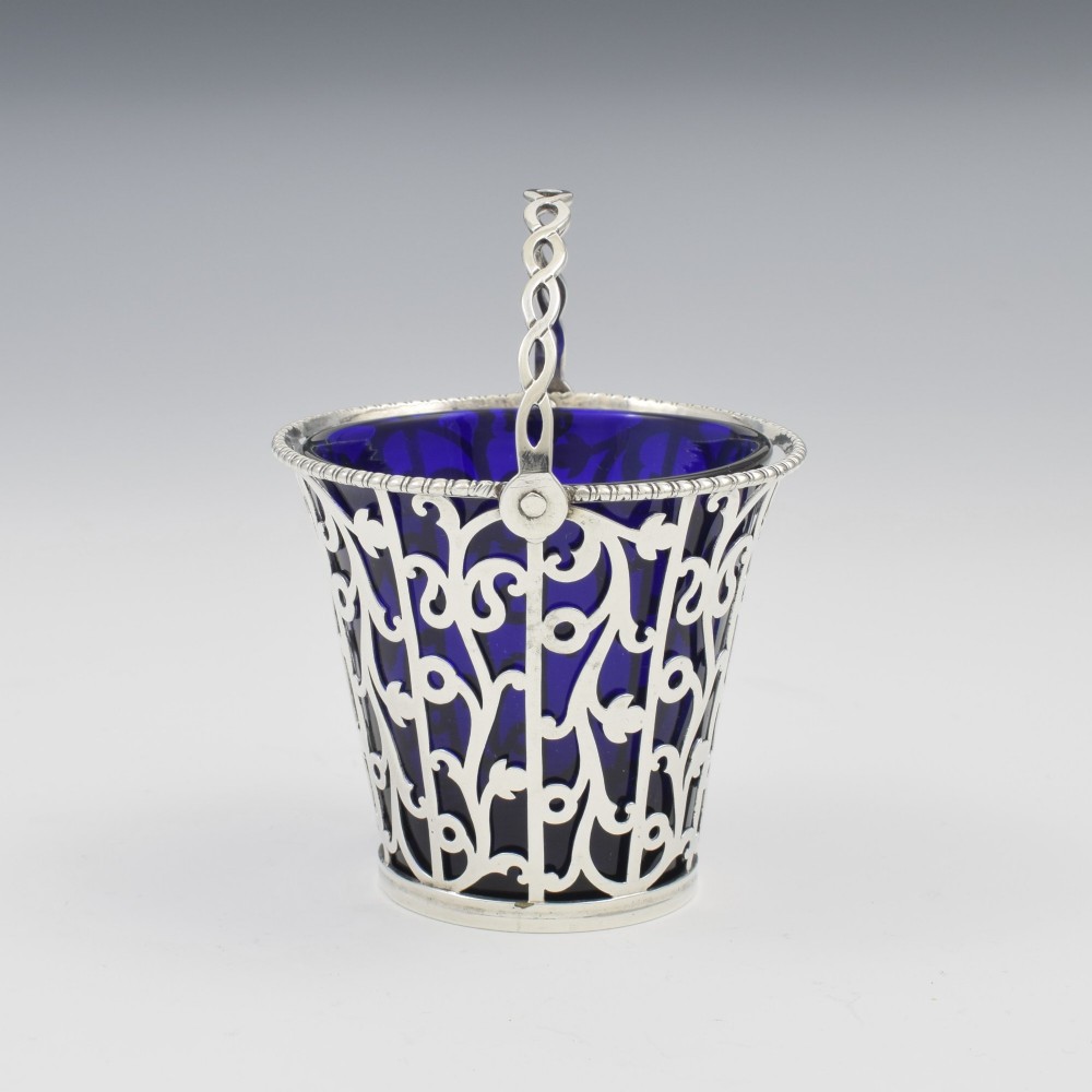 An 18th-century Georgian pierced sterling silver cream pail featuring intricate foliage scrollwork, a swing handle, and a removable cobalt blue glass liner. View VI