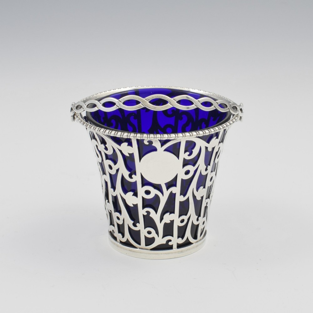 An 18th-century Georgian pierced sterling silver cream pail featuring intricate foliage scrollwork, a swing handle, and a removable cobalt blue glass liner. View VII