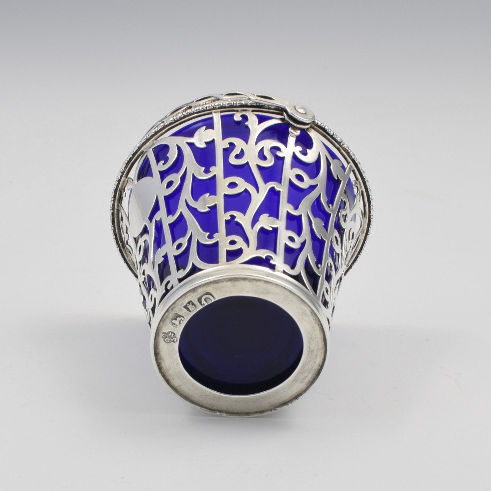 An 18th-century Georgian pierced sterling silver cream pail featuring intricate foliage scrollwork, a swing handle, and a removable cobalt blue glass liner. View VIII