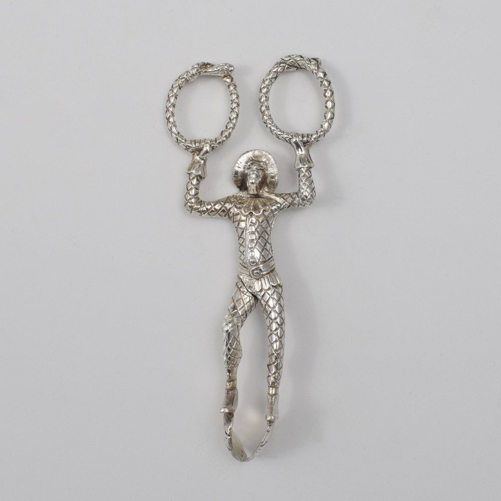 A George IV sterling silver novelty sugar tong designed as a Harlequin figure holding circular ring handles above its head. View II