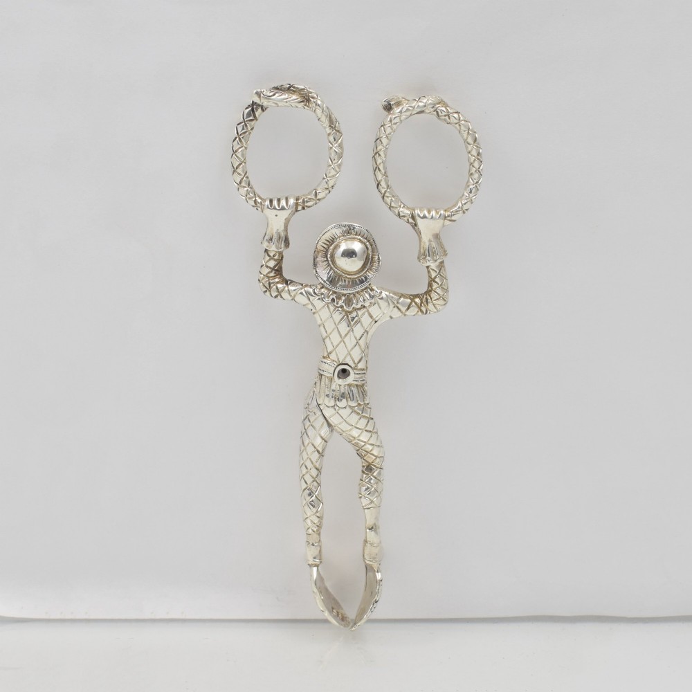 A George IV sterling silver novelty sugar tong designed as a Harlequin figure holding circular ring handles above its head. View IV
