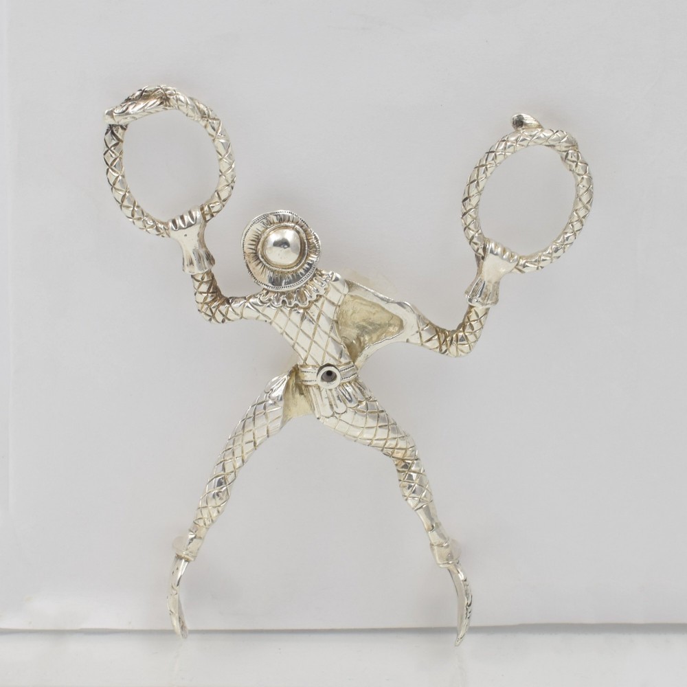 A George IV sterling silver novelty sugar tong designed as a Harlequin figure holding circular ring handles above its head. View V