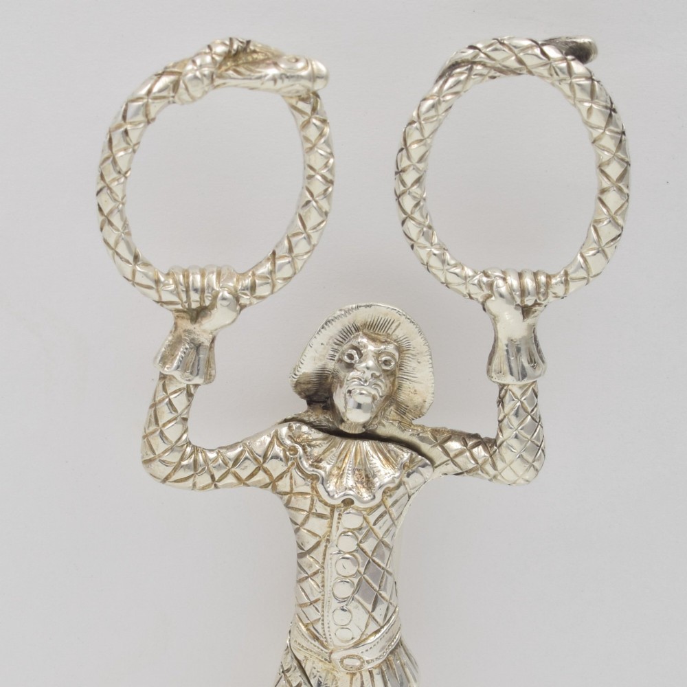 A George IV sterling silver novelty sugar tong designed as a Harlequin figure holding circular ring handles above its head. View VI