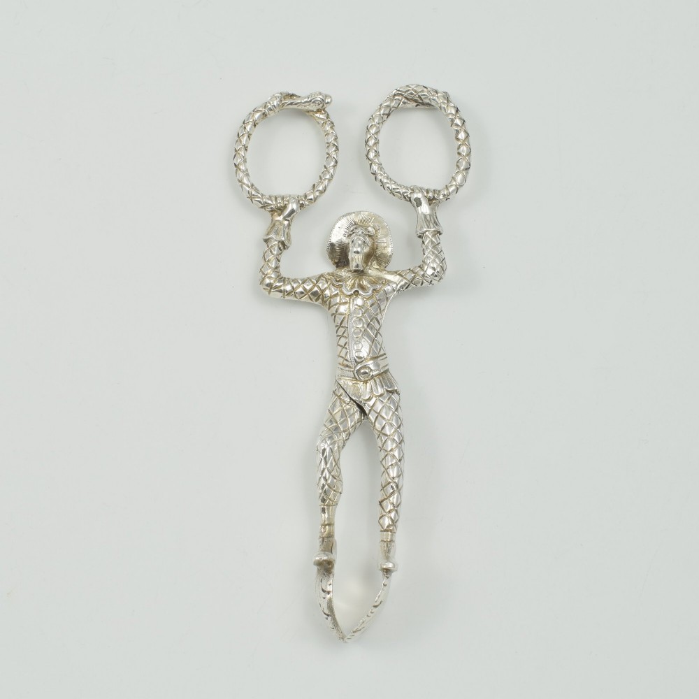 A George IV sterling silver novelty sugar tong designed as a Harlequin figure holding circular ring handles above its head. View IX