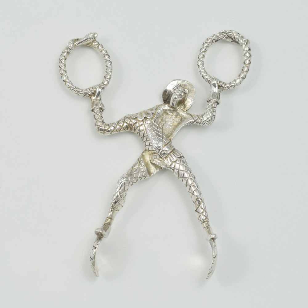 A George IV sterling silver novelty sugar tong designed as a Harlequin figure holding circular ring handles above its head. View X