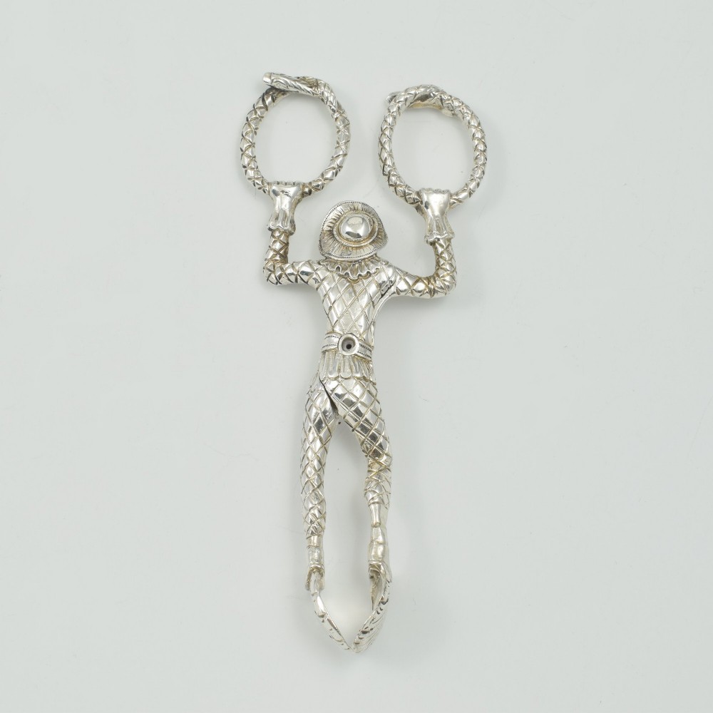 A George IV sterling silver novelty sugar tong designed as a Harlequin figure holding circular ring handles above its head. View XI