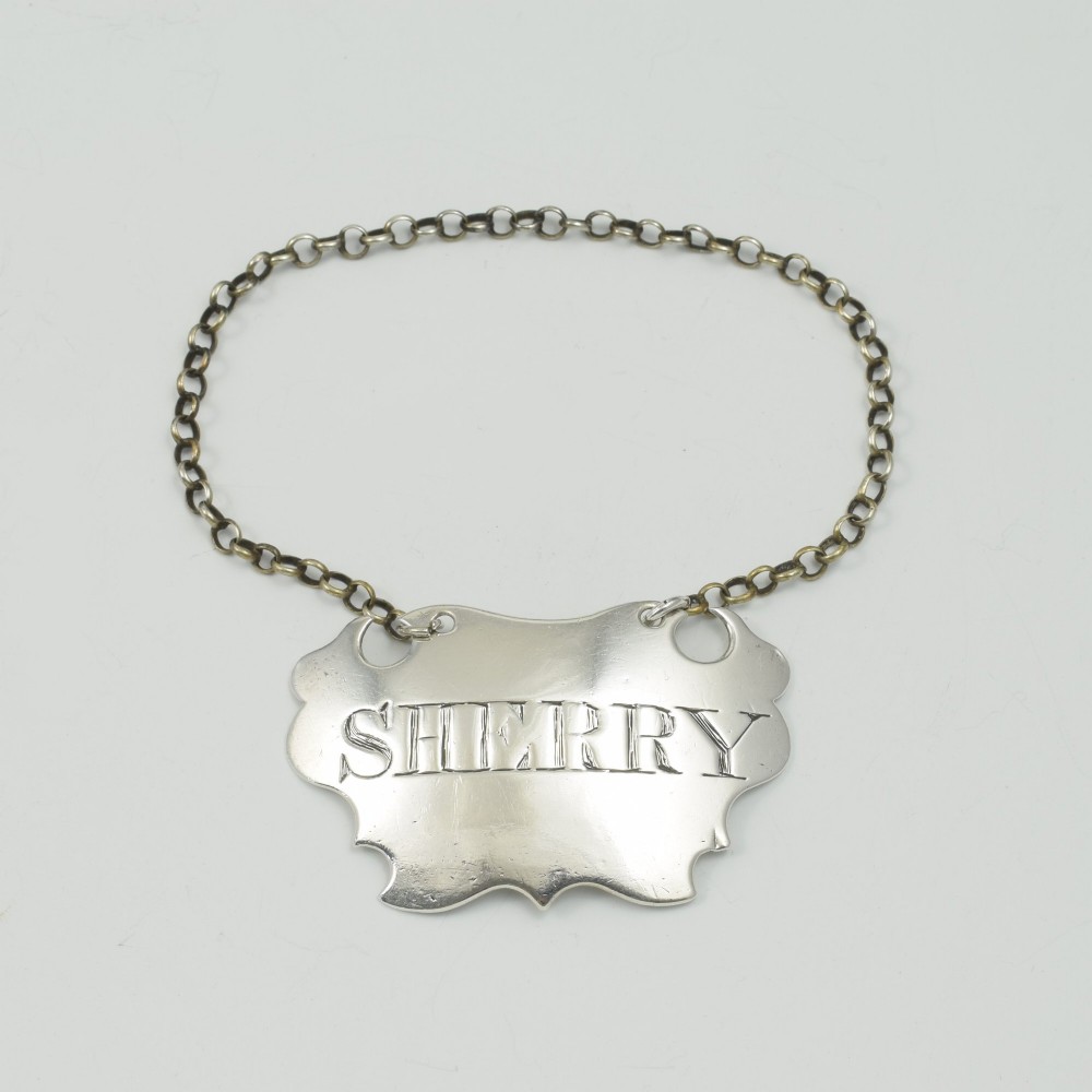 A Georgian sterling silver escutcheon-shaped decanter label engraved with the word SHERRY, featuring a suspension chain.