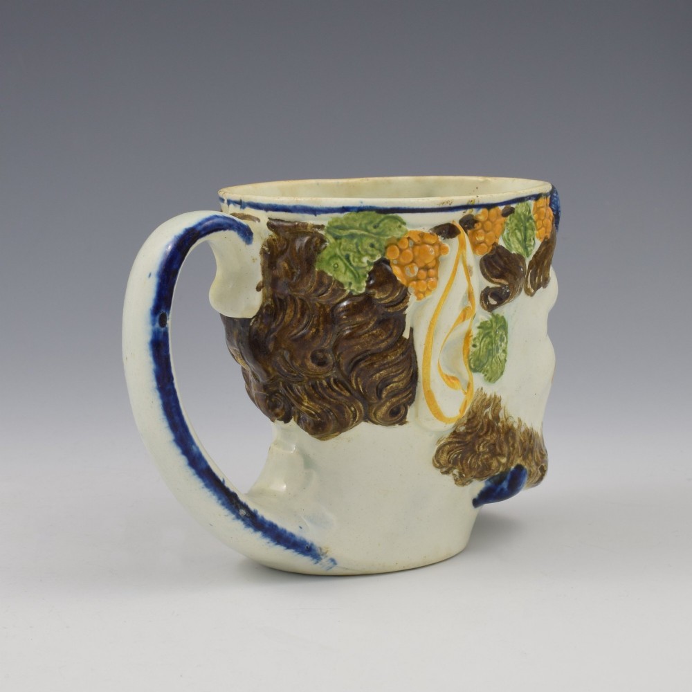 A late 18th-century pearlware ceramic mug formed as a satyrs head with relief-moulded beard, pointed ears, and grapevines in underglaze colours. View VIII