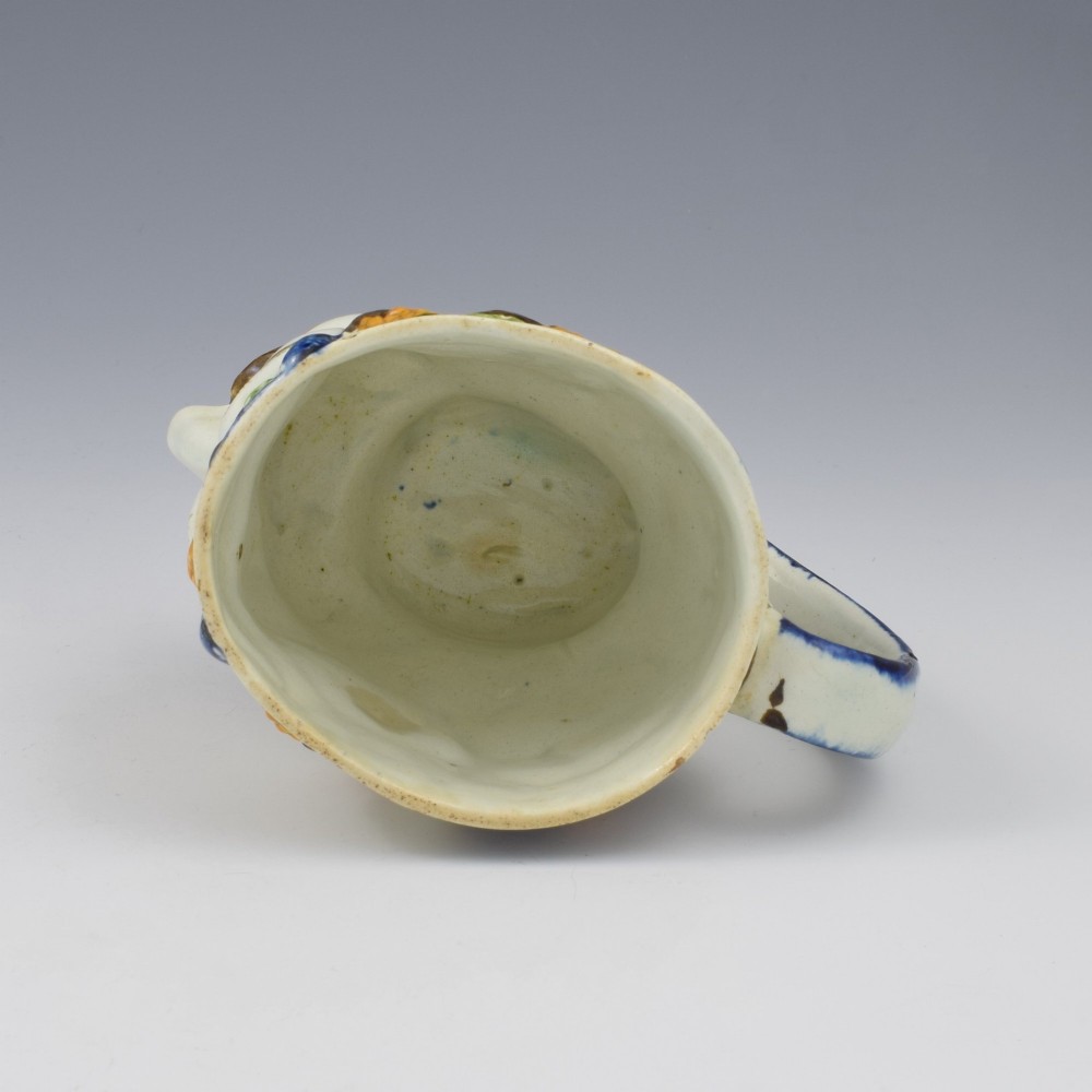 A late 18th-century pearlware ceramic mug formed as a satyrs head with relief-moulded beard, pointed ears, and grapevines in underglaze colours. View XII