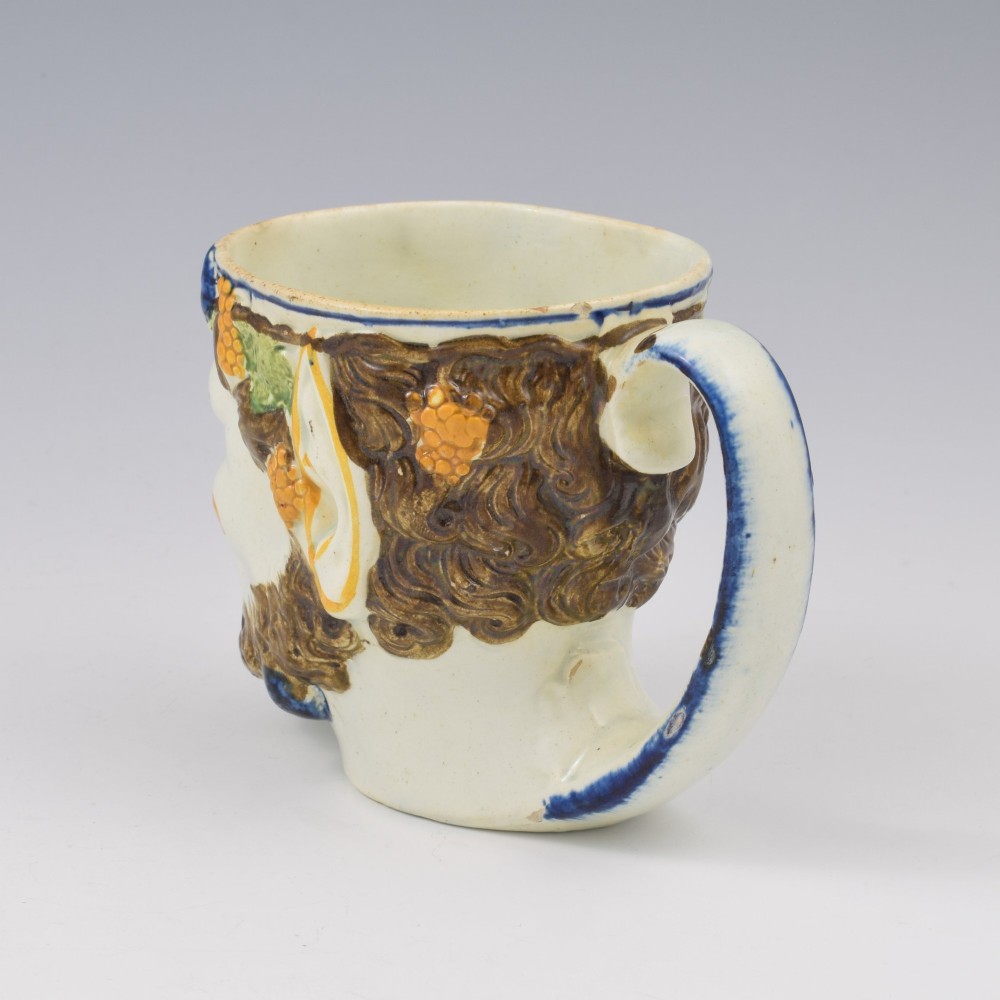 A late 18th-century pearlware ceramic mug formed as a satyrs head with relief-moulded beard, pointed ears, and grapevines in underglaze colours. View XIII