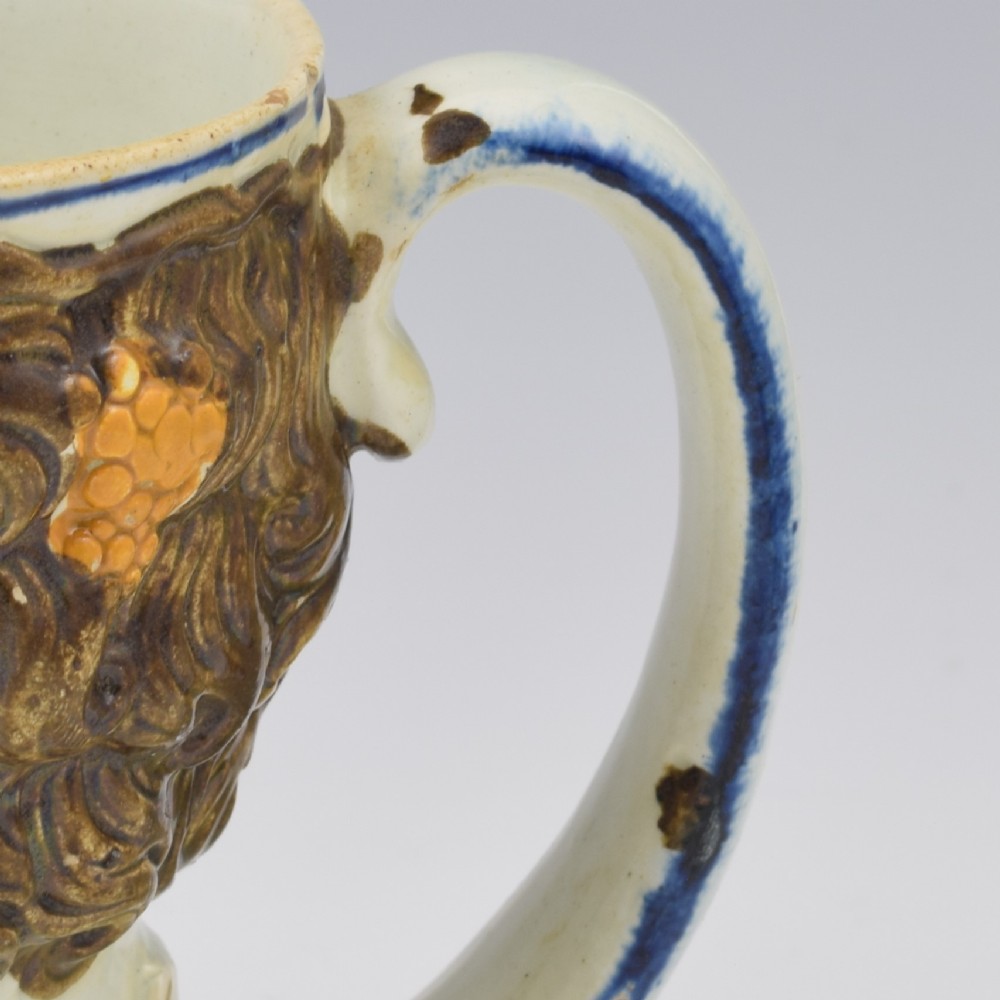 A late 18th-century pearlware ceramic mug formed as a satyrs head with relief-moulded beard, pointed ears, and grapevines in underglaze colours. View XIV