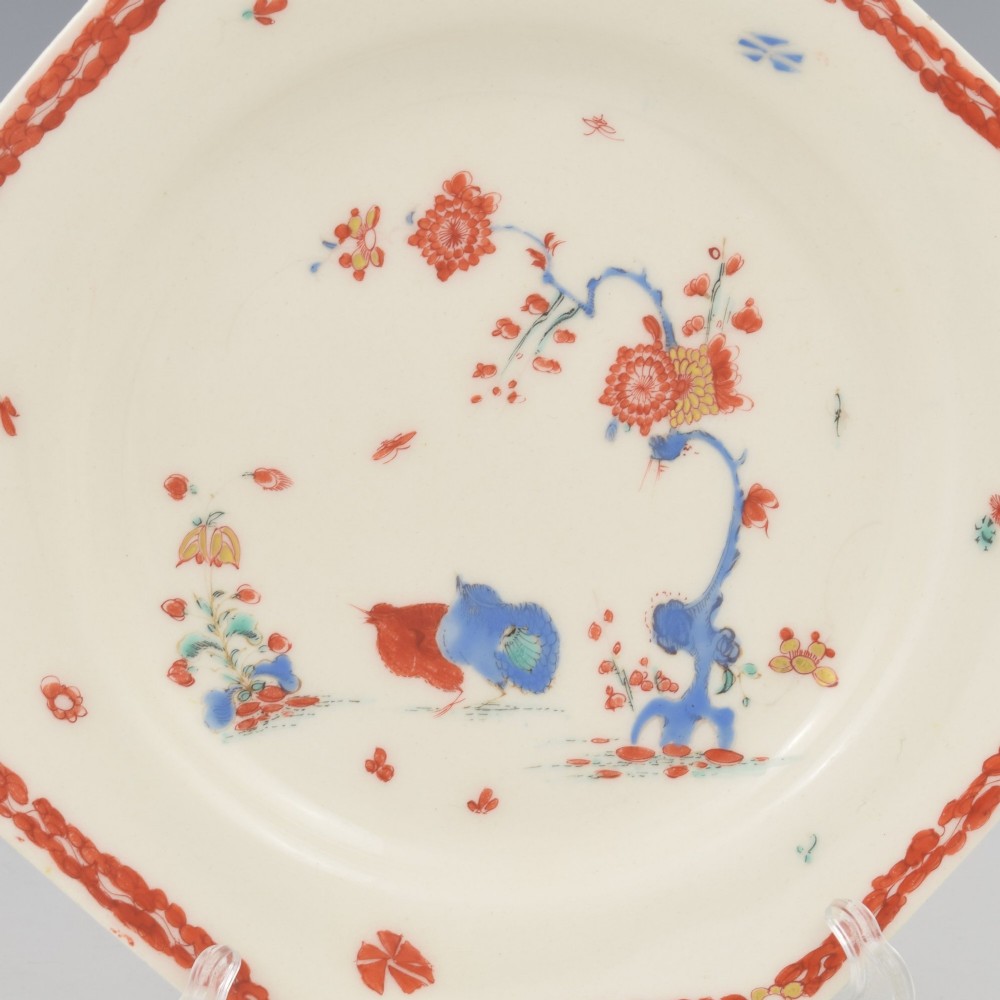 An 18th-century octagonal soft-paste porcelain plate decorated with iron-red and blue enamels showing two quails under flowering branches within a red scroll border. View II