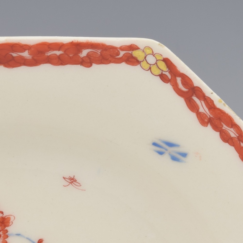 An 18th-century octagonal soft-paste porcelain plate decorated with iron-red and blue enamels showing two quails under flowering branches within a red scroll border. View V
