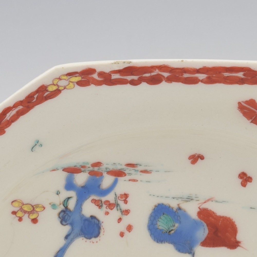 An 18th-century octagonal soft-paste porcelain plate decorated with iron-red and blue enamels showing two quails under flowering branches within a red scroll border. View VI