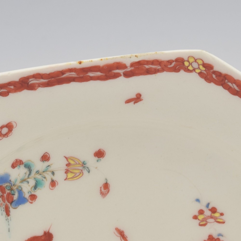 An 18th-century octagonal soft-paste porcelain plate decorated with iron-red and blue enamels showing two quails under flowering branches within a red scroll border. View IX