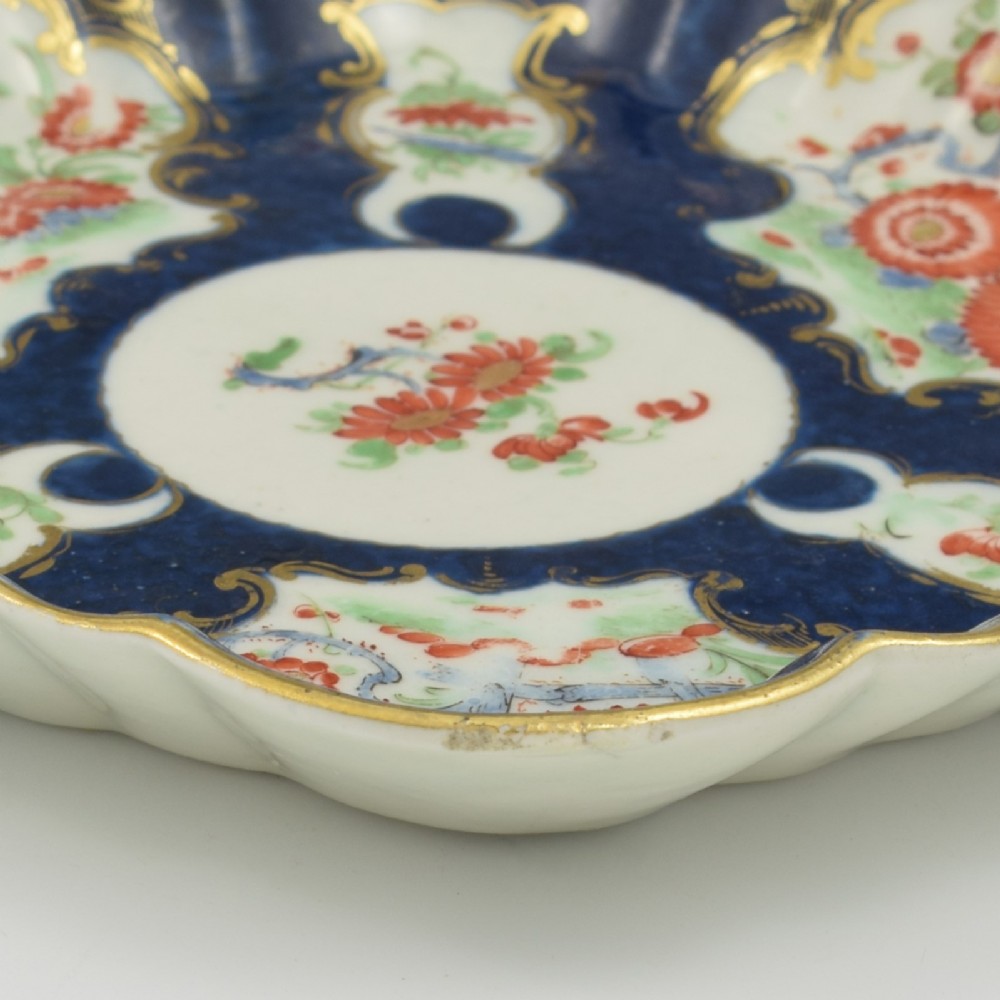 A scalloped Dr Wall Worcester porcelain teapot stand featuring a hand-painted blue scale ground, gilded rococo cartouches, and colourful Kakiemon-style floral motifs. View VII