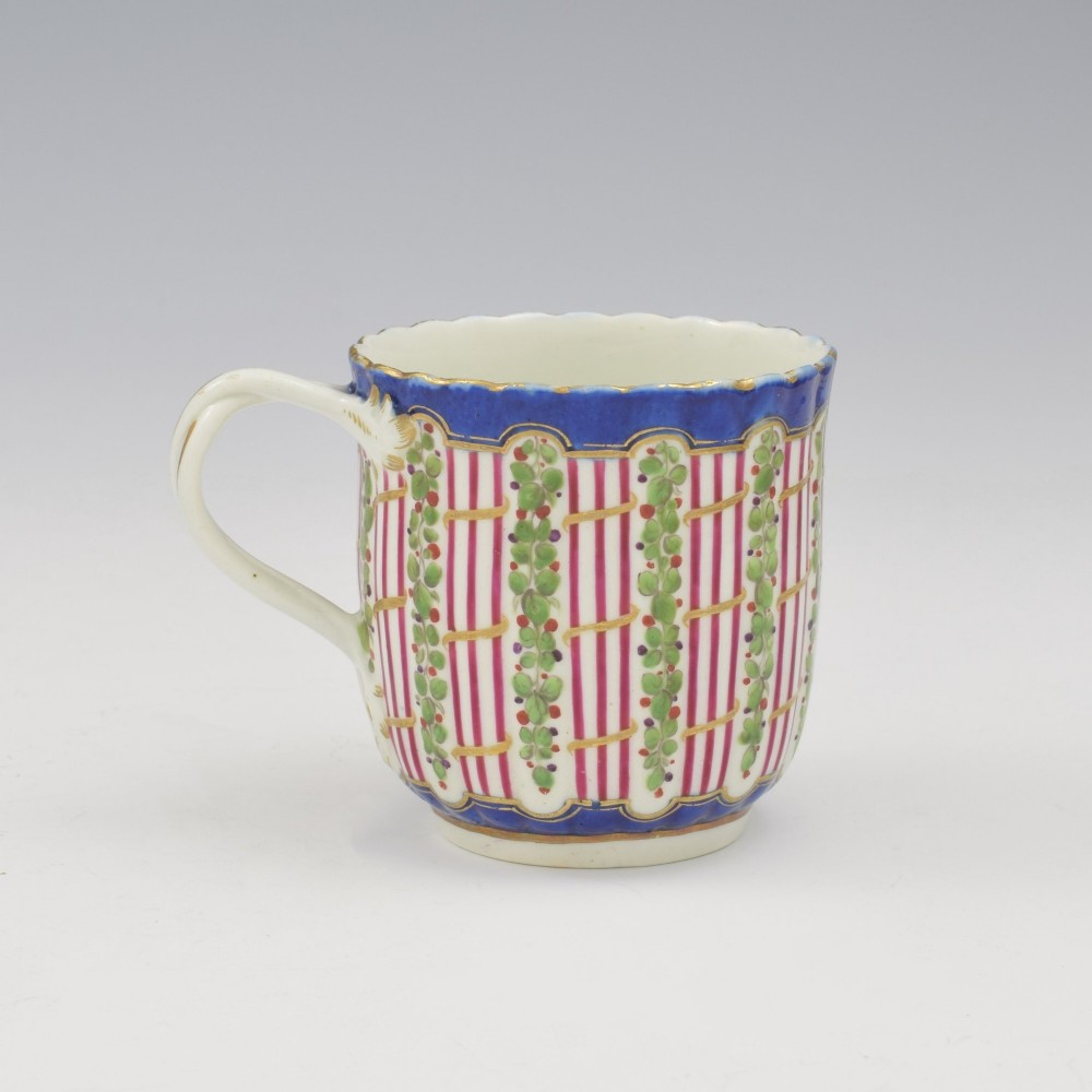 An 18th-century soft-paste porcelain coffee cup and saucer with fluted edges, featuring a cobalt blue border, gilt highlights, and a painted green hop trellis pattern. View V