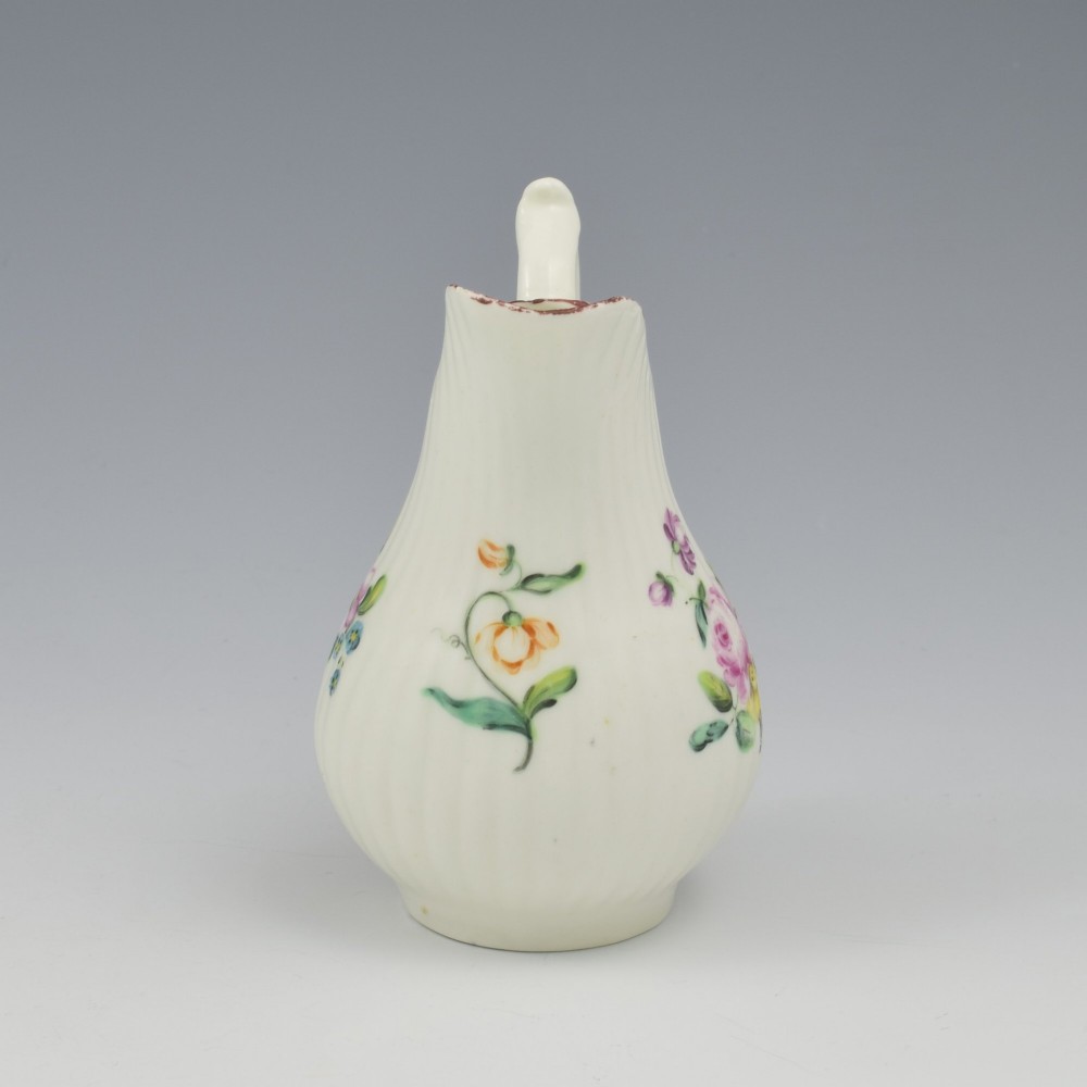 An eighteenth-century English soft-paste porcelain cream jug with vertical fluting, hand-painted floral motifs, and a looped handle. View X