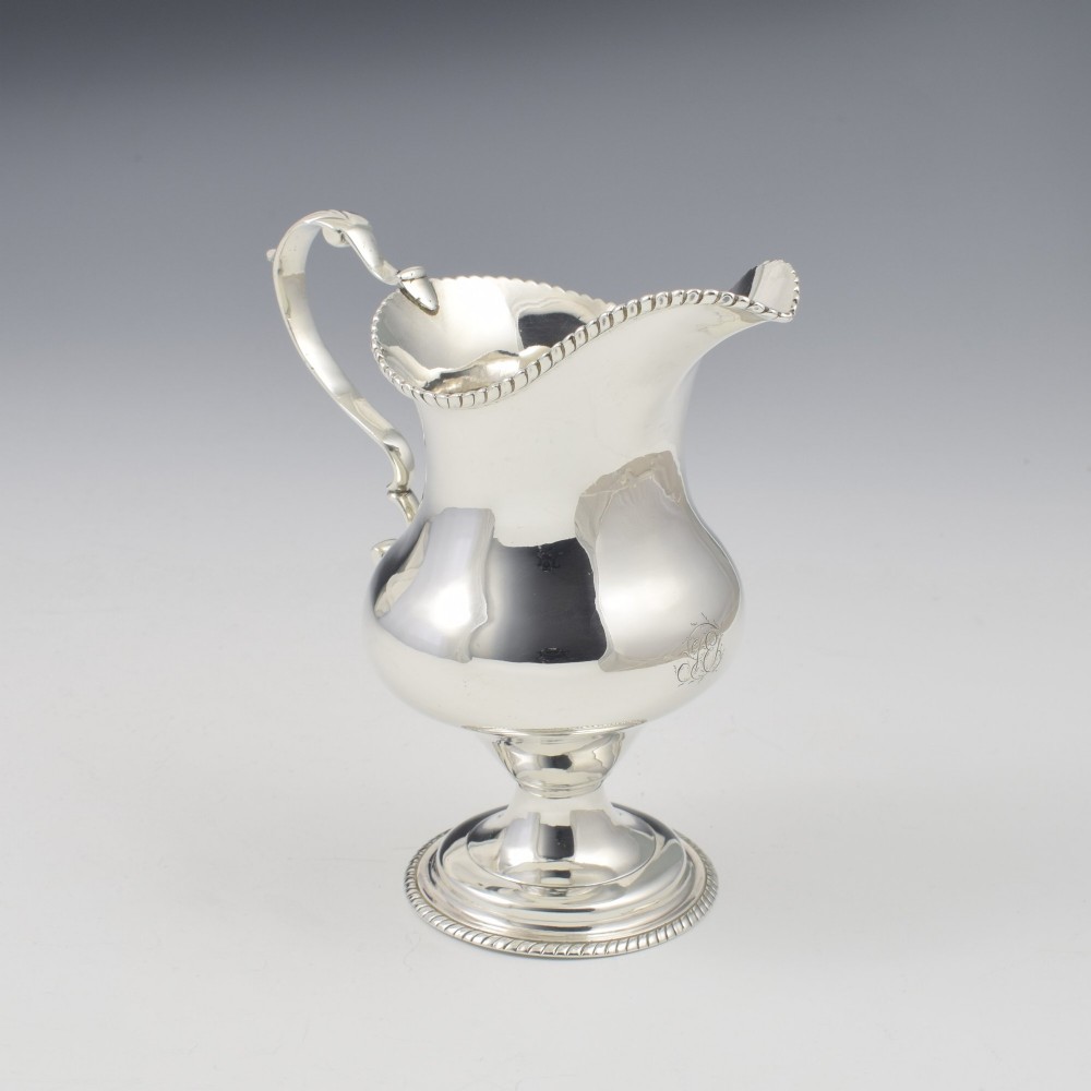 A Georgian sterling silver milk jug featuring a baluster body, pedestal foot, beaded rim, and double-scroll handle. View V