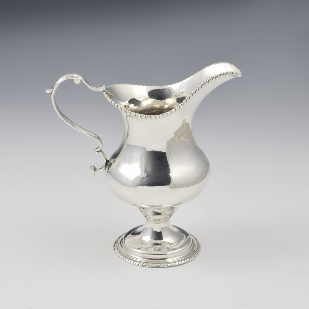 A Georgian sterling silver milk jug featuring a baluster body, pedestal foot, beaded rim, and double-scroll handle. View VI