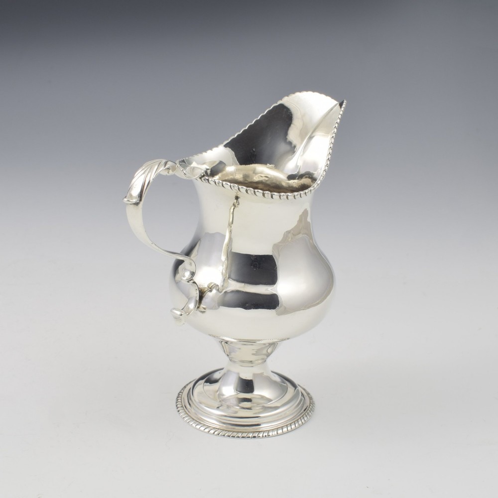 A Georgian sterling silver milk jug featuring a baluster body, pedestal foot, beaded rim, and double-scroll handle. View VII