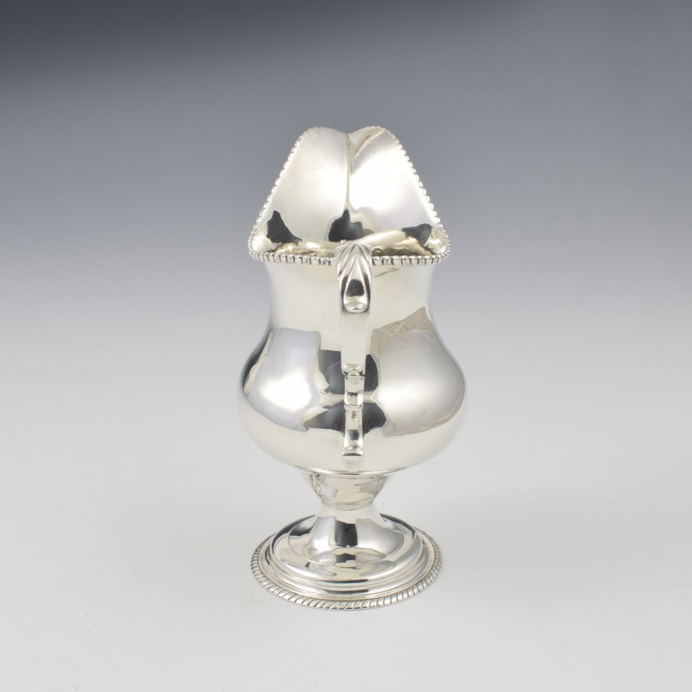 A Georgian sterling silver milk jug featuring a baluster body, pedestal foot, beaded rim, and double-scroll handle. View VIII