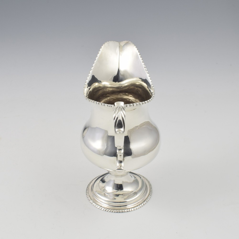 A Georgian sterling silver milk jug featuring a baluster body, pedestal foot, beaded rim, and double-scroll handle. View IX