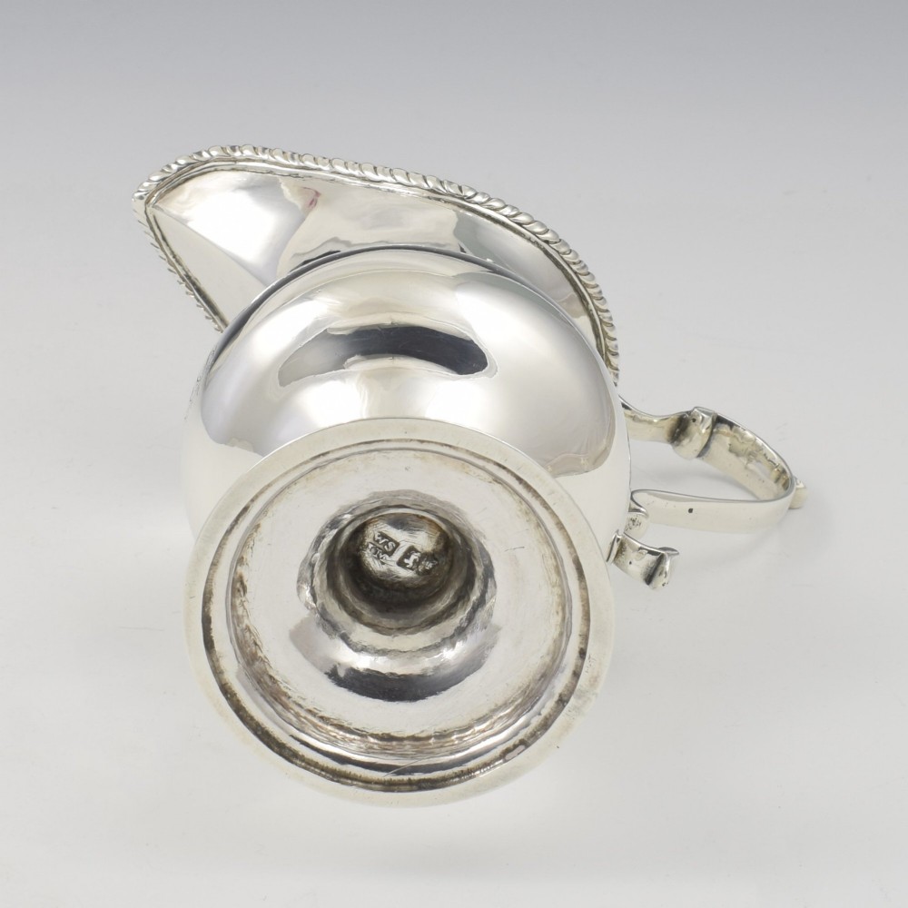 A Georgian sterling silver milk jug featuring a baluster body, pedestal foot, beaded rim, and double-scroll handle. View XI