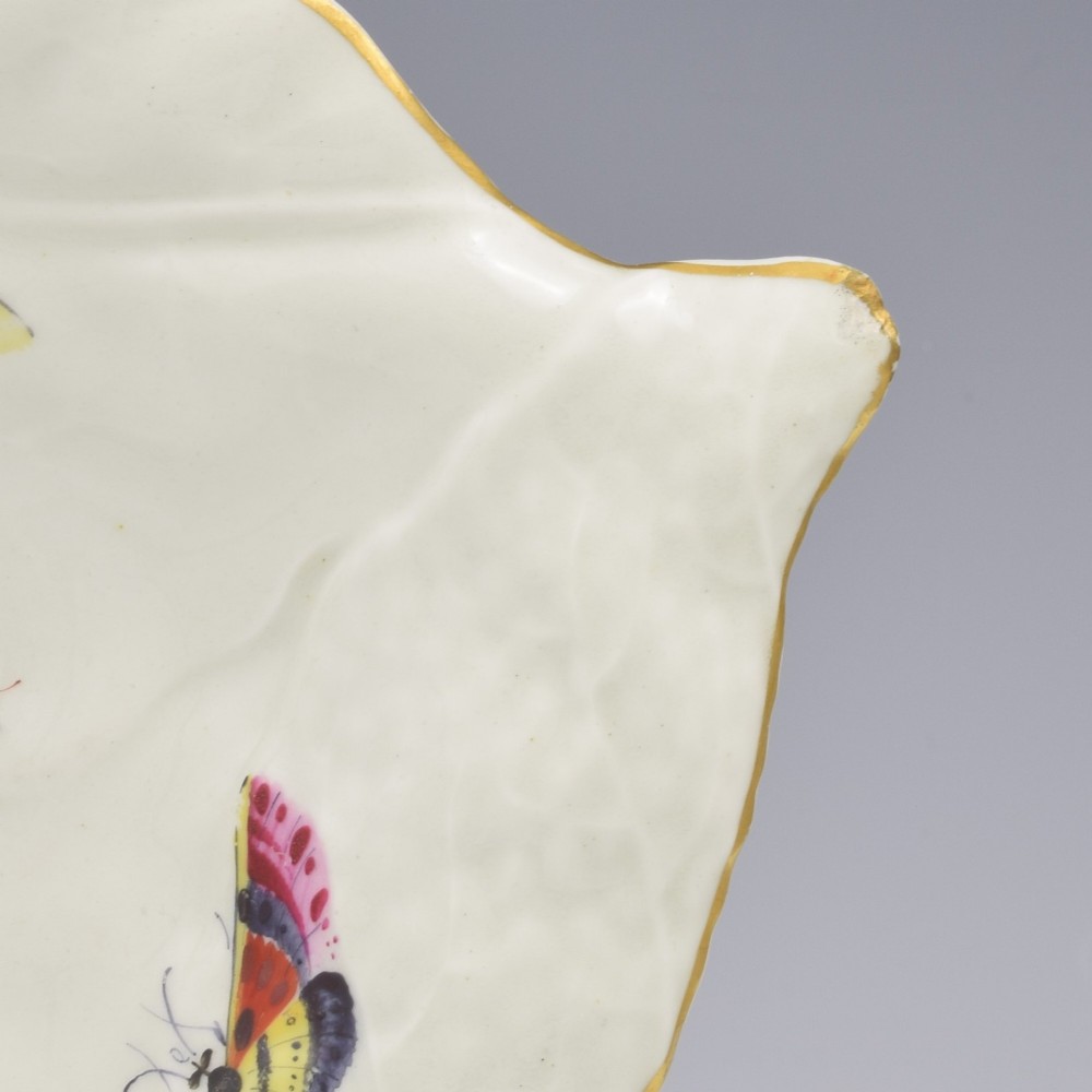 An eighteenth-century leaf-moulded soft-paste porcelain dish featuring central hand-painted fancy birds, surrounding butterflies, a pink stalk handle, and a gilded edge. View VII