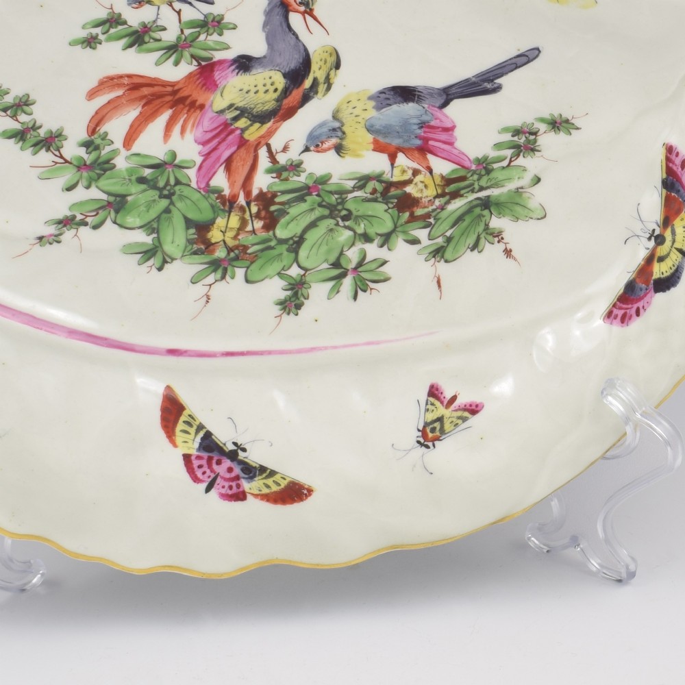 An eighteenth-century leaf-moulded soft-paste porcelain dish featuring central hand-painted fancy birds, surrounding butterflies, a pink stalk handle, and a gilded edge. View VIII