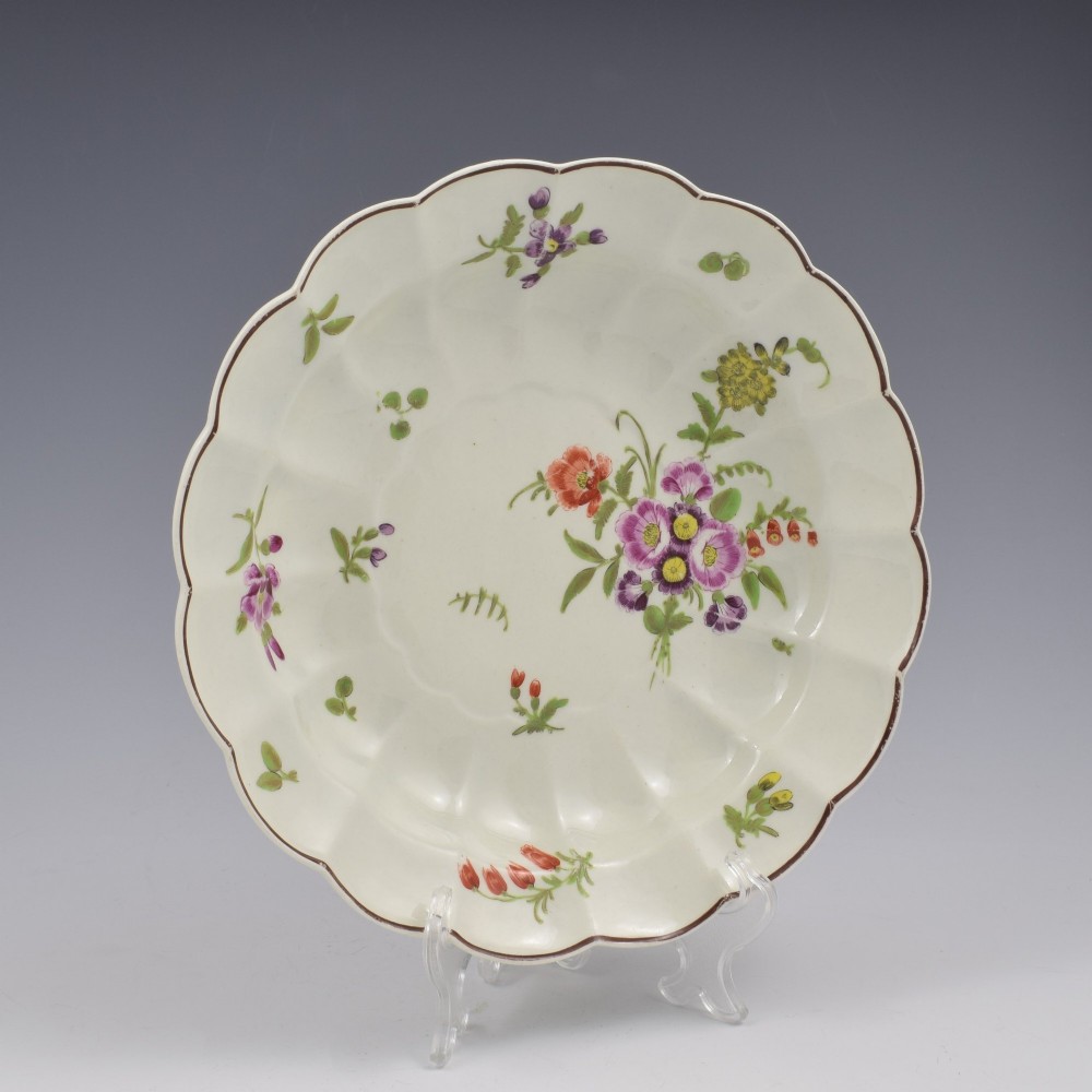 An 18th-century lobed soft-paste porcelain plate decorated with hand-painted polychrome floral sprays and a brown line rim. View II