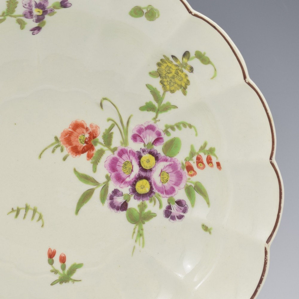 An 18th-century lobed soft-paste porcelain plate decorated with hand-painted polychrome floral sprays and a brown line rim. View V