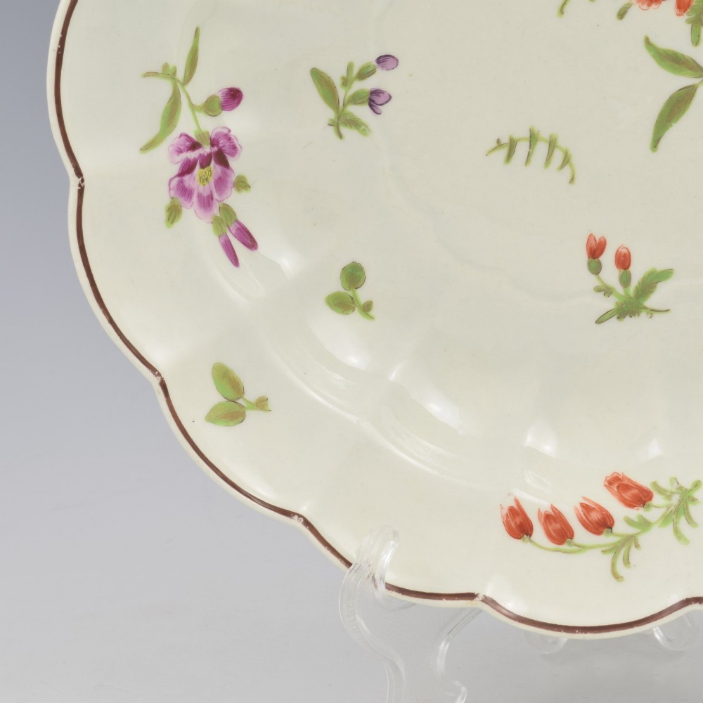 An 18th-century lobed soft-paste porcelain plate decorated with hand-painted polychrome floral sprays and a brown line rim. View VI