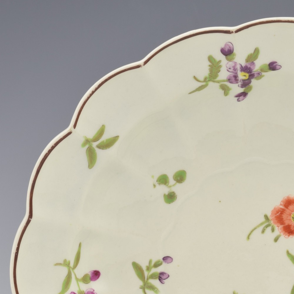 An 18th-century lobed soft-paste porcelain plate decorated with hand-painted polychrome floral sprays and a brown line rim. View VII