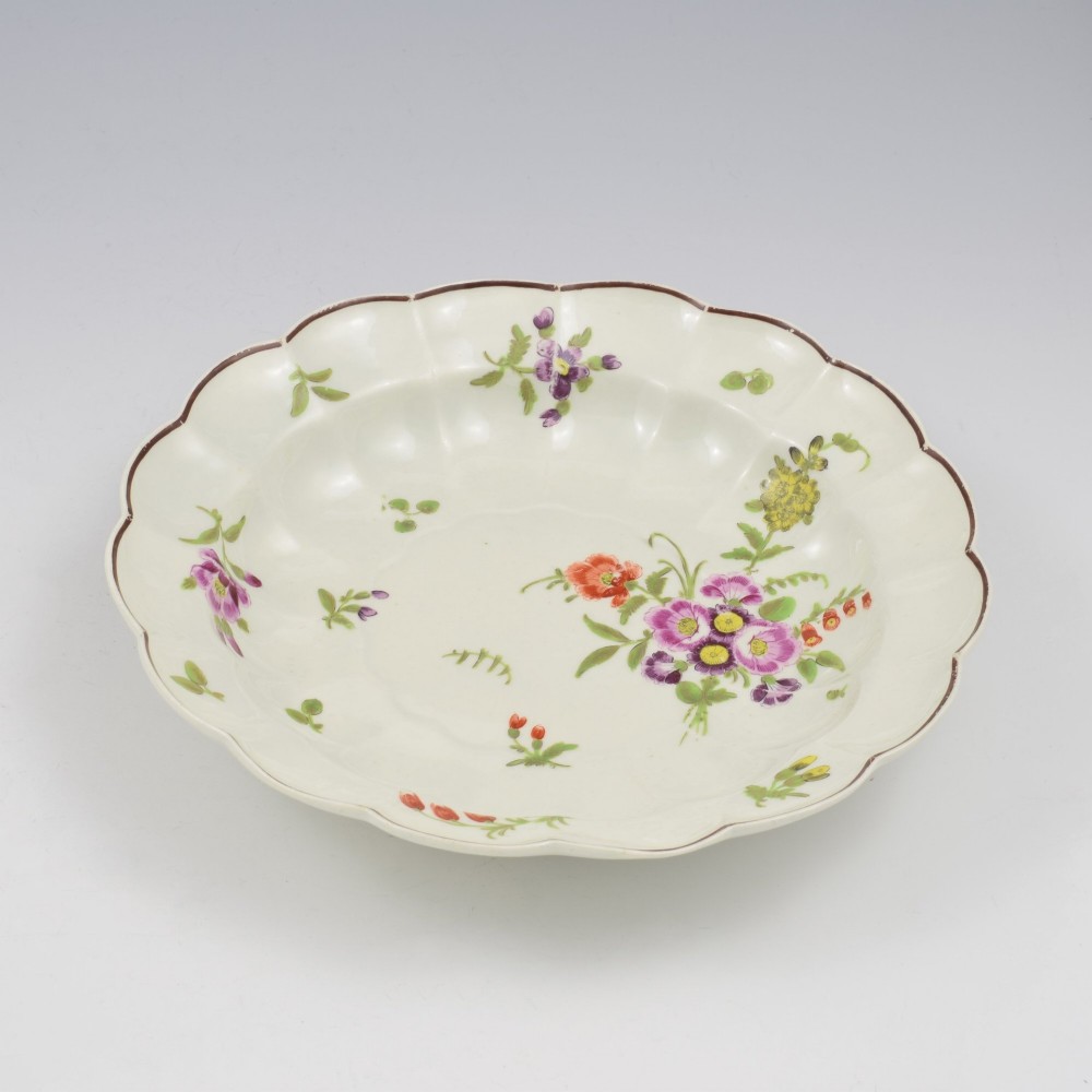An 18th-century lobed soft-paste porcelain plate decorated with hand-painted polychrome floral sprays and a brown line rim. View IX
