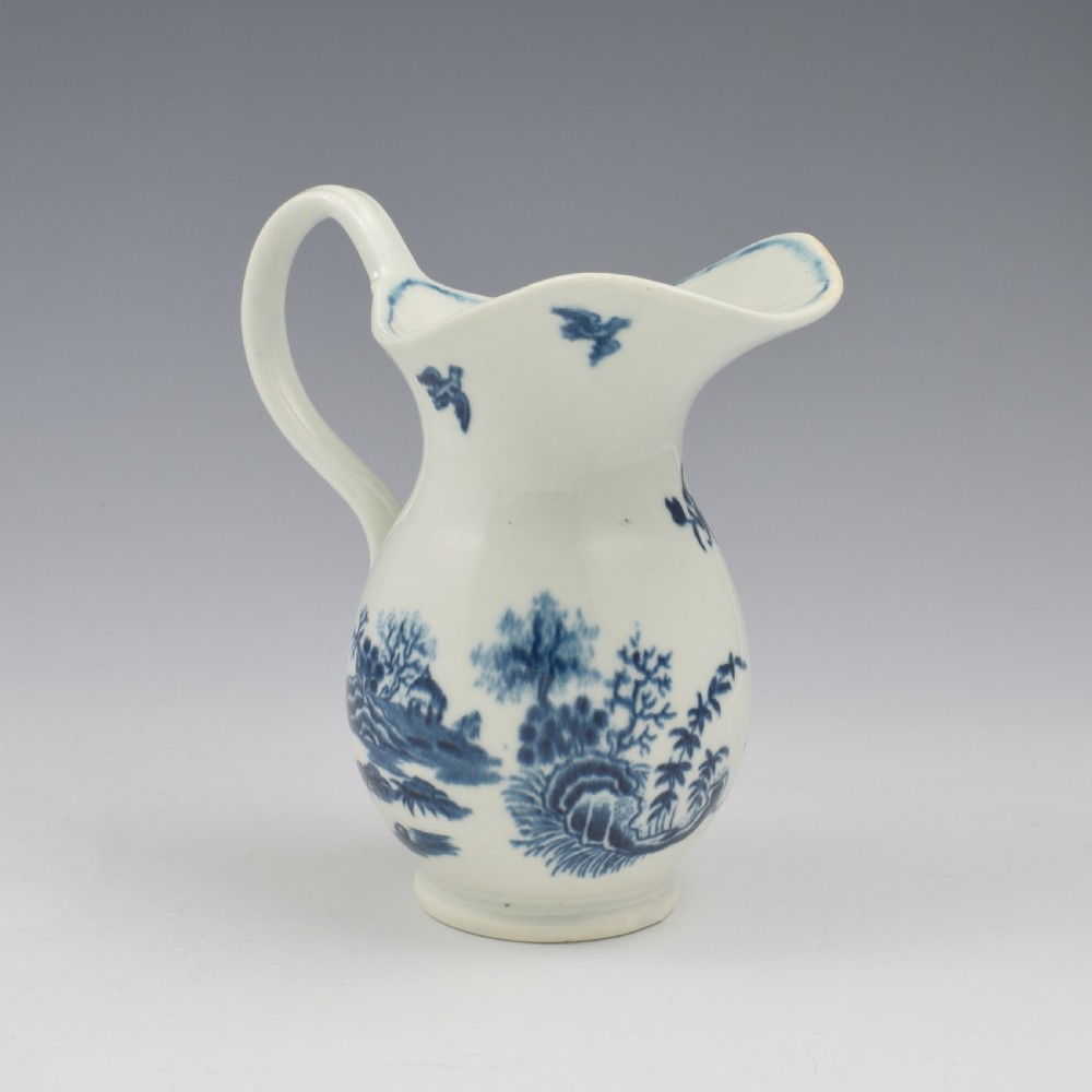 An 18th-century blue and white Worcester porcelain milk ewer featuring a flared spout, loop handle, and hand-painted floral motifs. View V