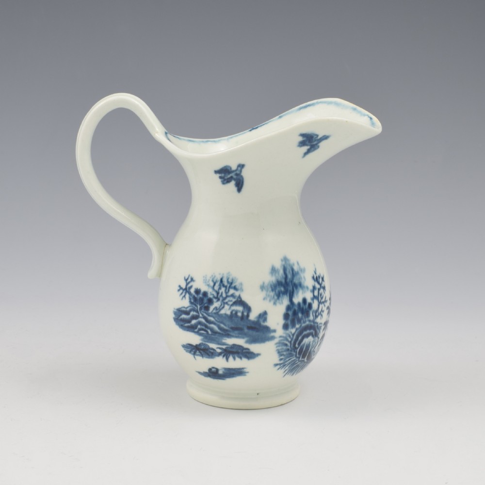 An 18th-century blue and white Worcester porcelain milk ewer featuring a flared spout, loop handle, and hand-painted floral motifs. View VI