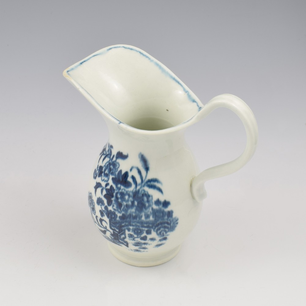 An 18th-century blue and white Worcester porcelain milk ewer featuring a flared spout, loop handle, and hand-painted floral motifs. View X