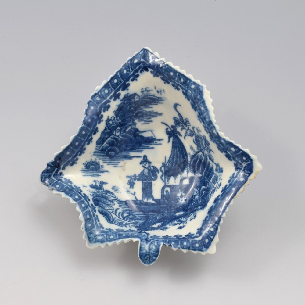 An 18th-century blue and white Caughley soft-paste porcelain pickle dish shaped like a leaf with a serrated rim and printed with a Oriental landscape pattern.